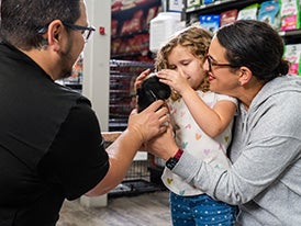Man in black shirt helping little girl pet a Guinea pig with her mom standing behind her inside of a pet supermarket store